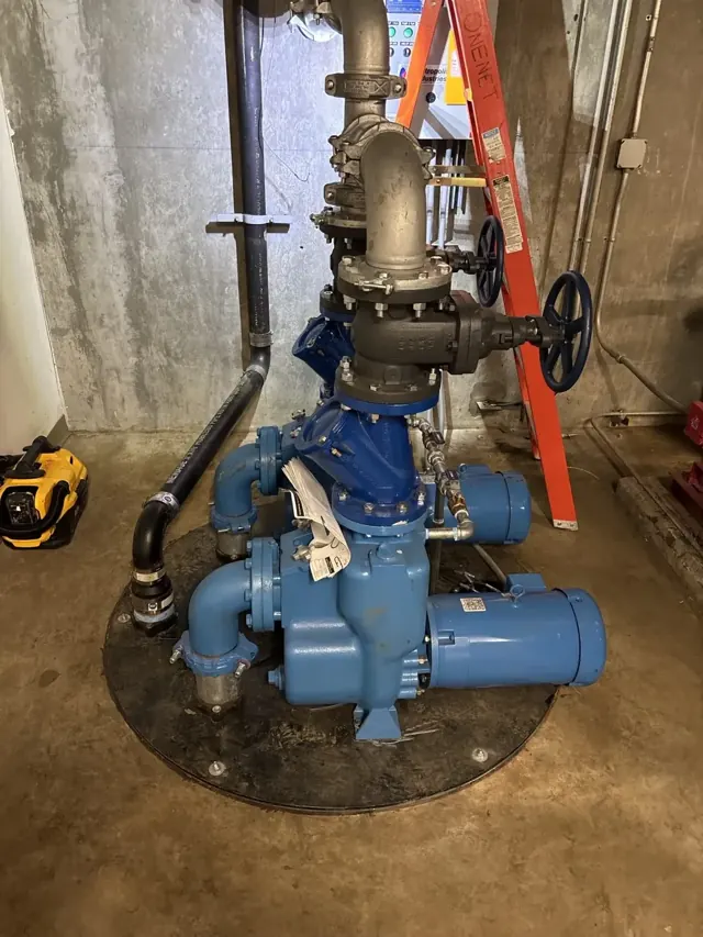 Large blue commercial pumps and valves in a concrete mechanical room