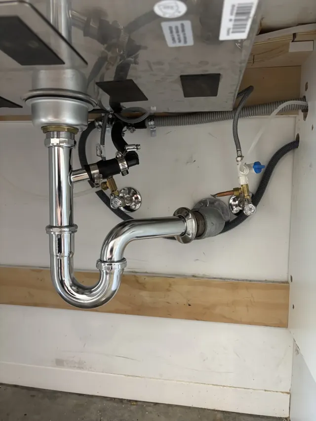 The same kitchen sink after repair: a clean new chrome P-trap and drain line